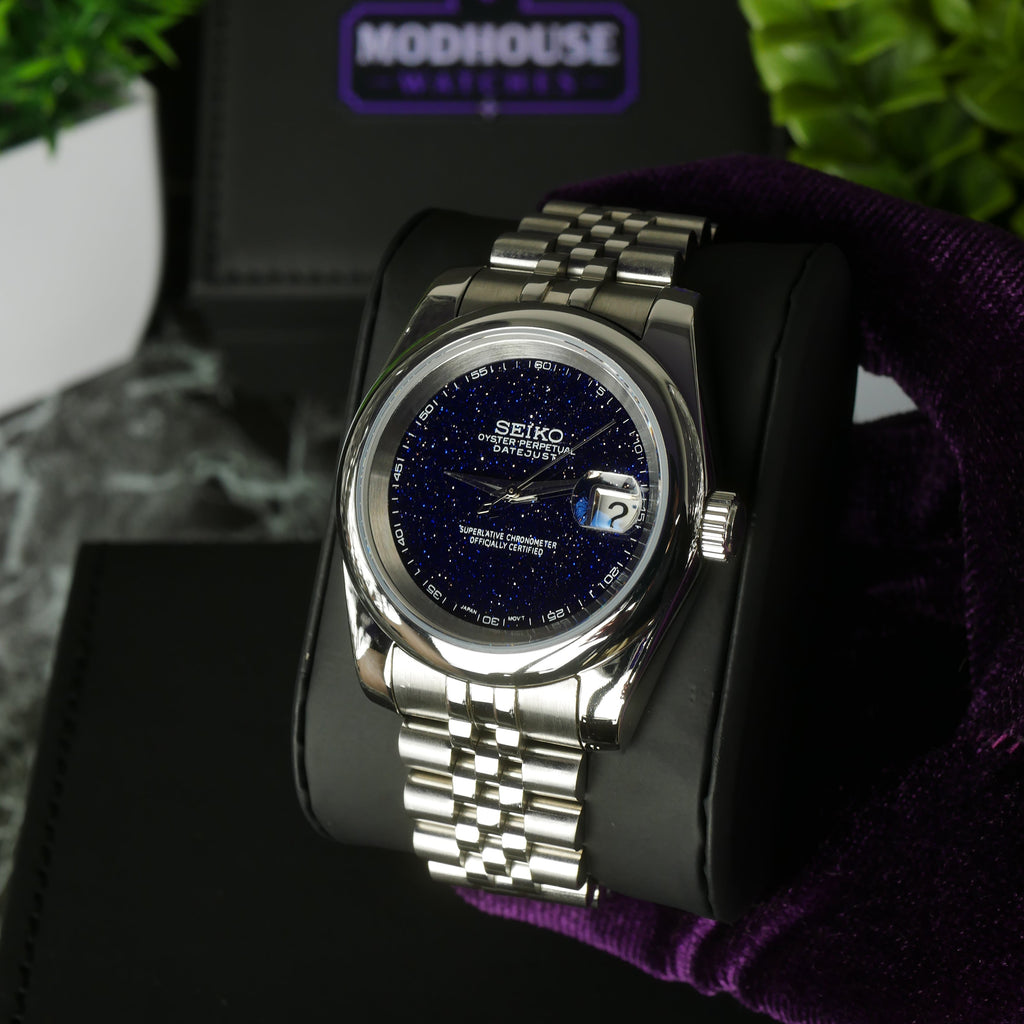 Silver watch with dark blue face on a black stand, brand logo visible