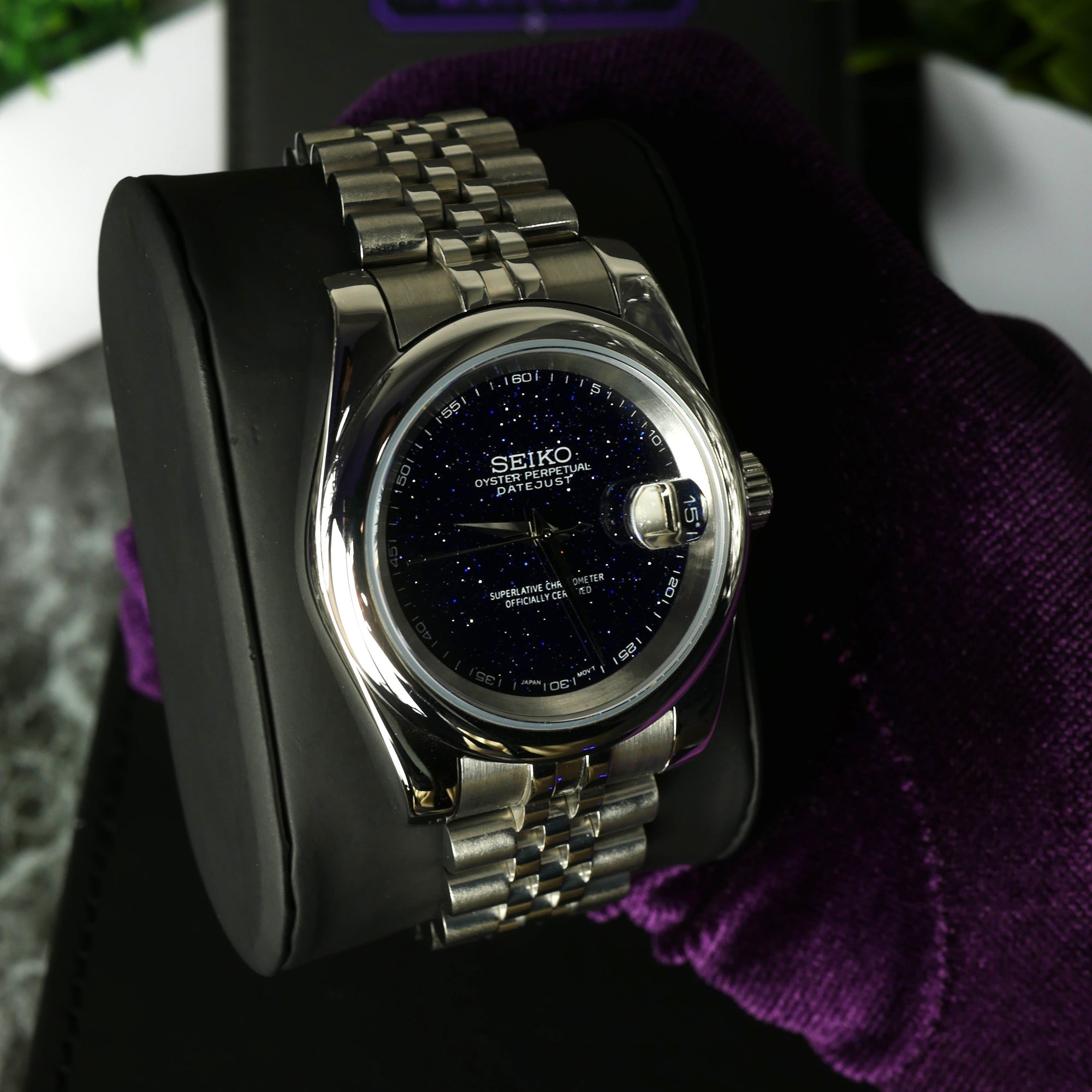 Seiko watch held by a gloved hand with a blurred 'MODHOUSE' logo in the background