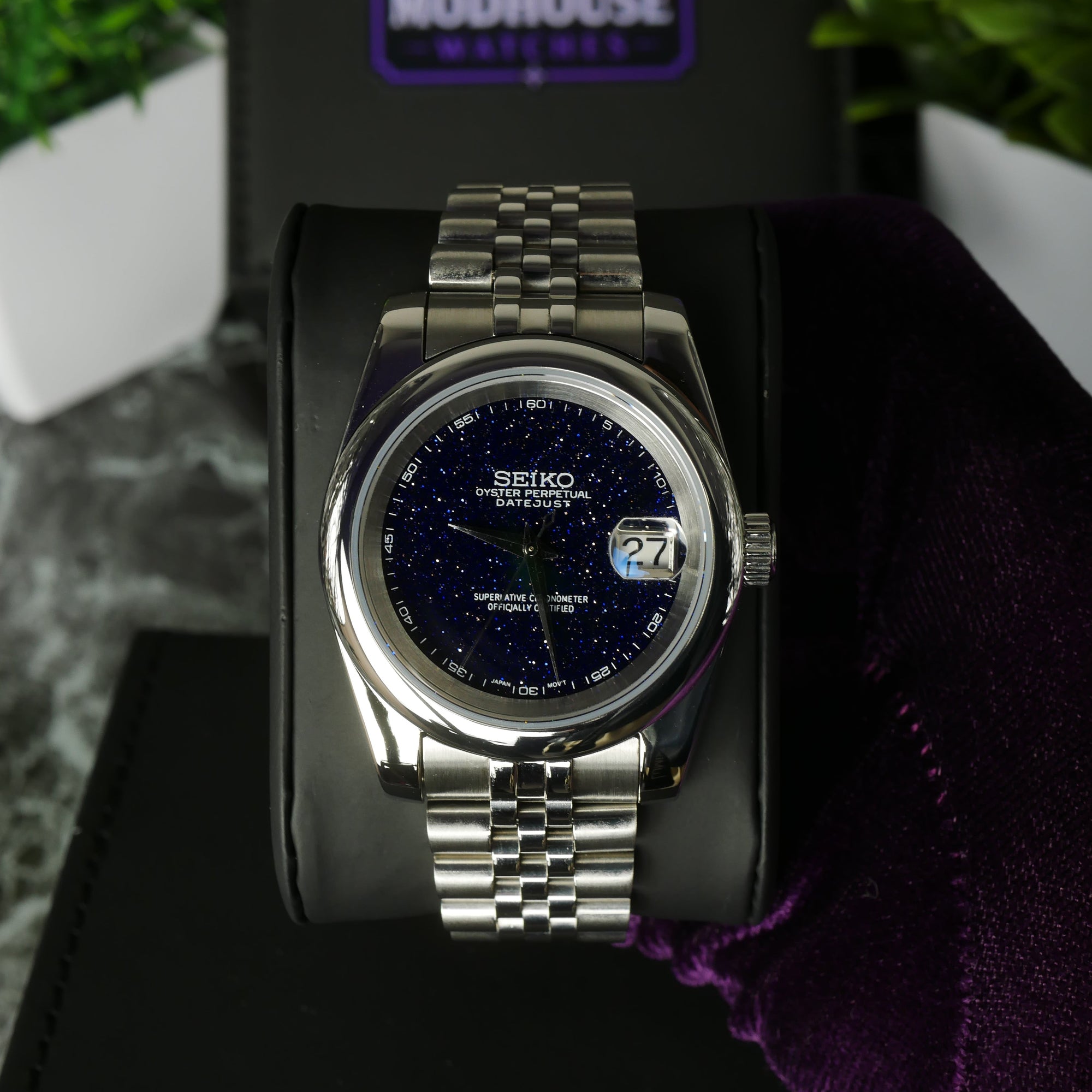 Silver Seiko watch on a black stand with a blurred background