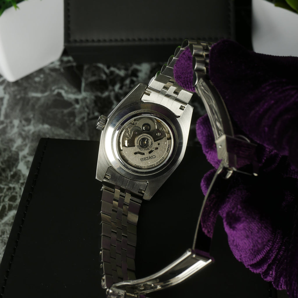 Close-up of a silver watch with a visible brand logo on a dark surface.